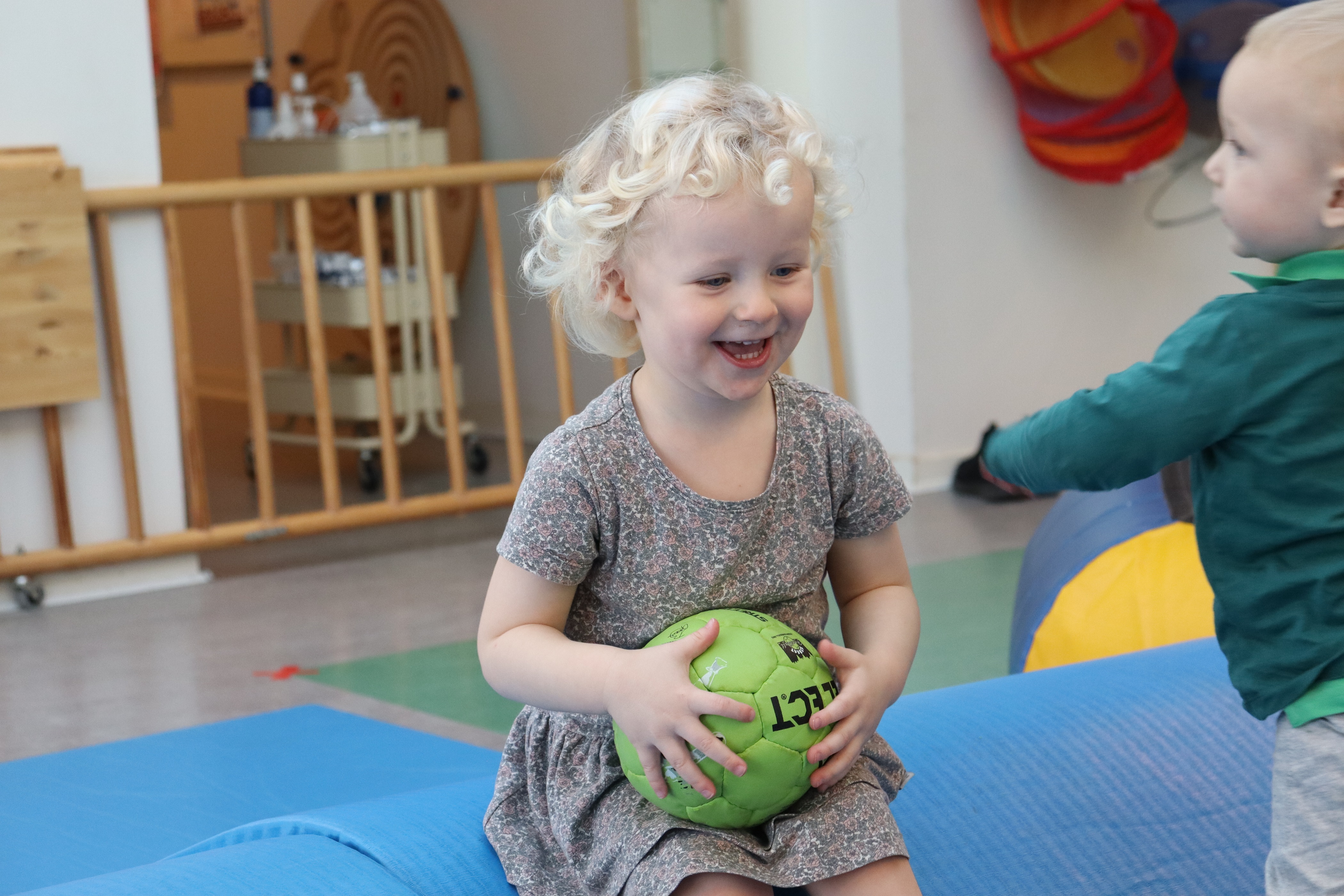Glad og smilende vuggestue barn, som sidder med en bold