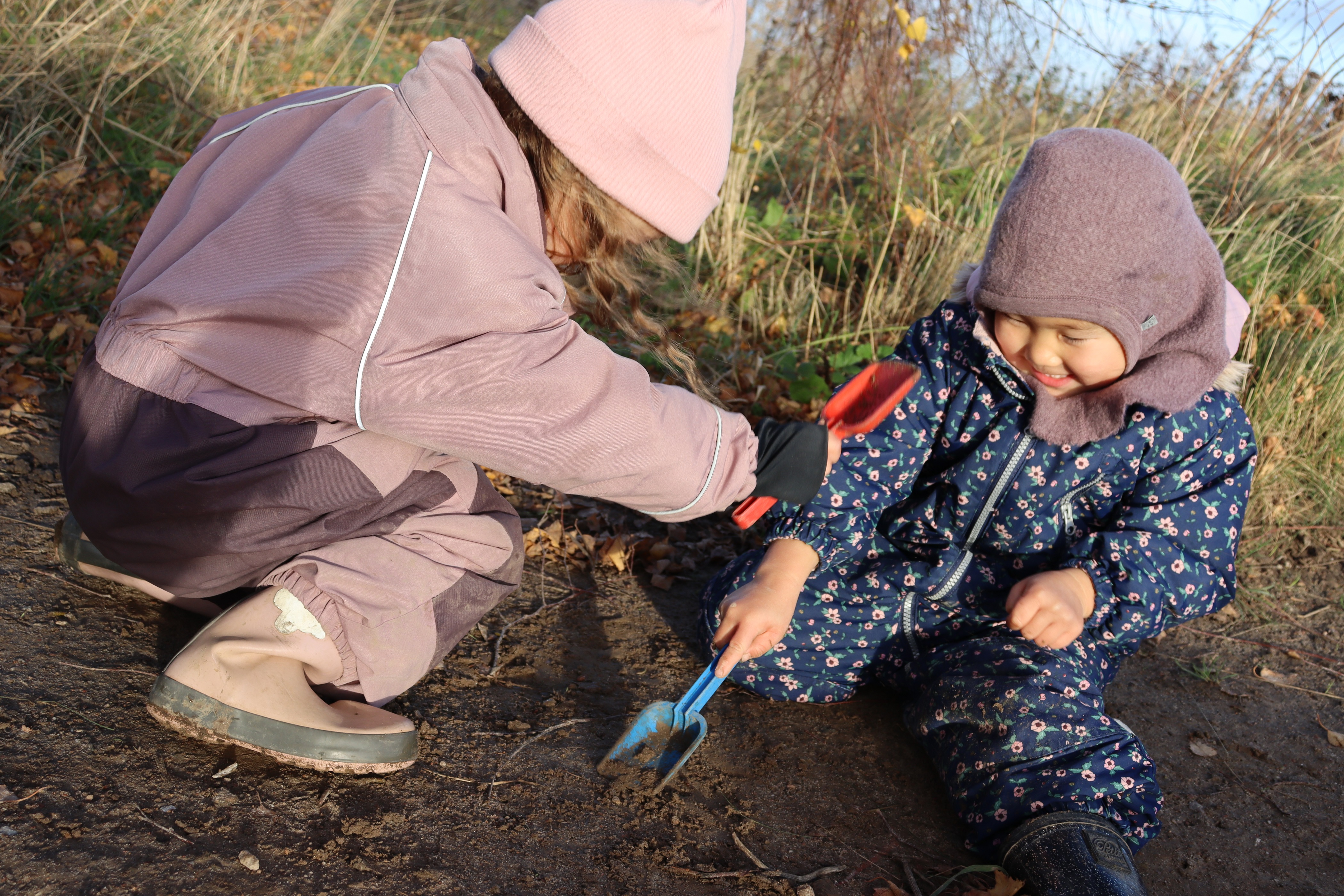 Børnehave børn undenfor, hvor de graver med små skeer. Stort smil